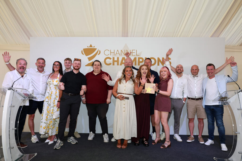 Group of people on a stage posing and smiling at a Chanel Champions event backdrop with raised hands