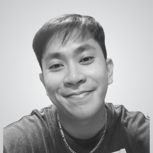 Smiling man taking a selfie in grayscale, wearing a chain necklace and a dark shirt.