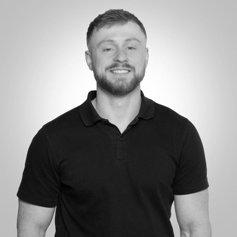 Smiling man with short hair and a beard, wearing a black polo shirt, posed for a head-and-shoulders portrait against a gray gradient background.
