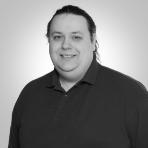 Smiling man with shoulder-length hair in a dark polo shirt, posing for a headshot against a light gray background.