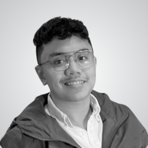 Smiling man with short dark hair and glasses wearing a white shirt and jacket, posed against a light gradient background.