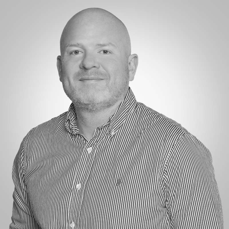 Head-and-shoulders portrait of a bald man with light stubble, wearing a striped button-down shirt, facing the camera with a subtle smile.