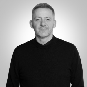 Head-and-shoulders portrait of a middle-aged man with short hair and stubble wearing a black sweater, looking at the camera.
