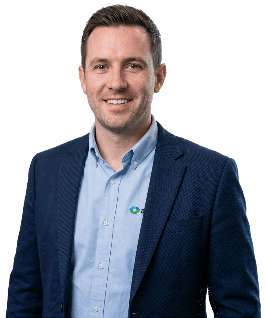 Portrait of a smiling man in a navy blazer and light blue shirt with a small logo on the chest, posed for a professional headshot.